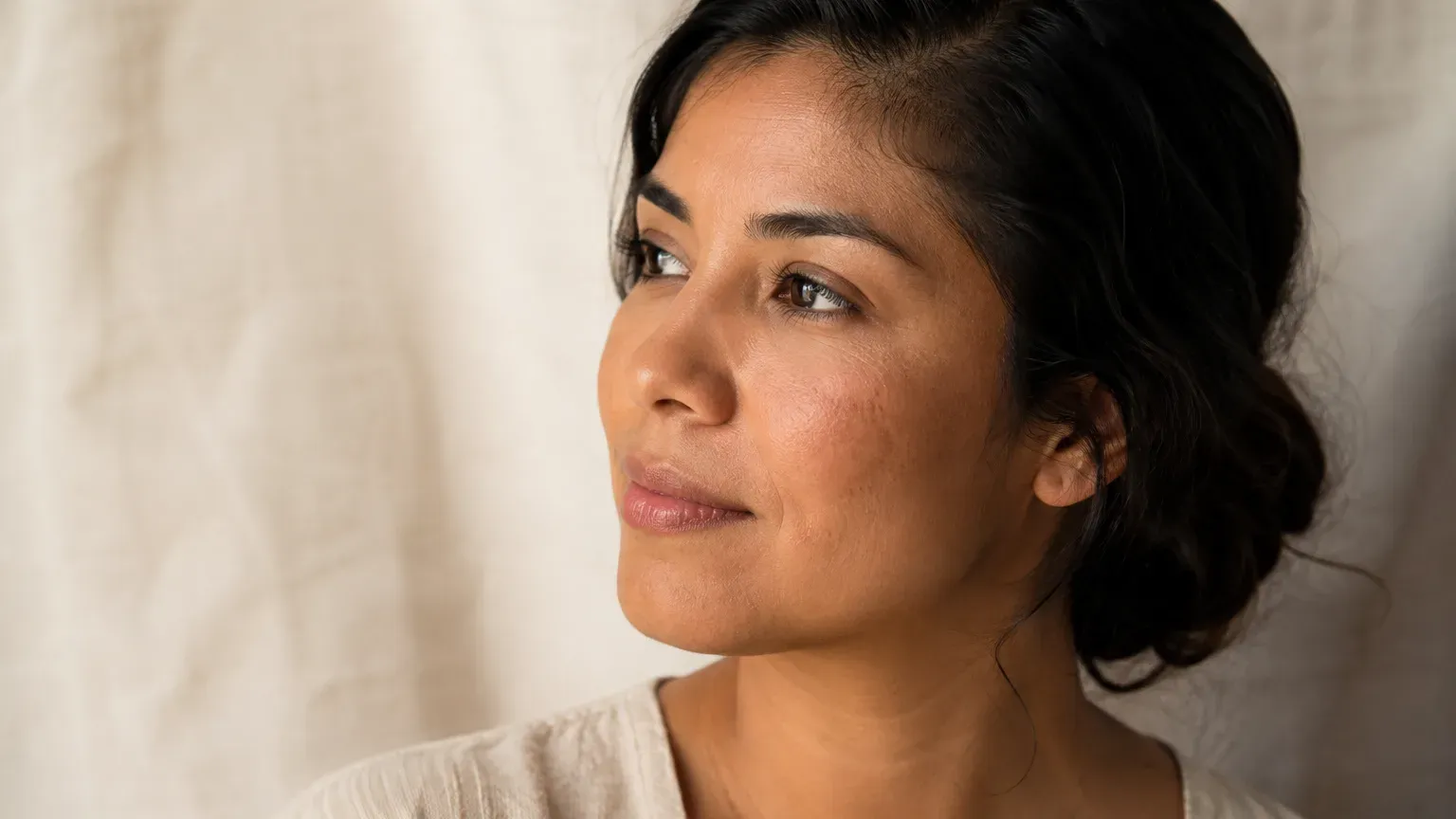 A close portrait of a person's cheekbone and upper lip in soft window light; Fitzpatrick IV, Latina skin.